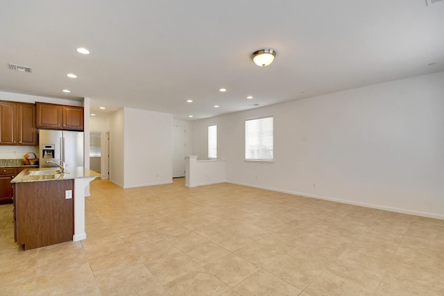 kitchen featuring sink, light tile floors, light stone counters, a center island with sink, and stainless steel refrigerator with ice dispenser