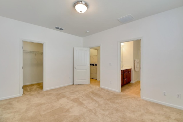 unfurnished bedroom featuring a closet, light colored carpet, ensuite bath, and a spacious closet