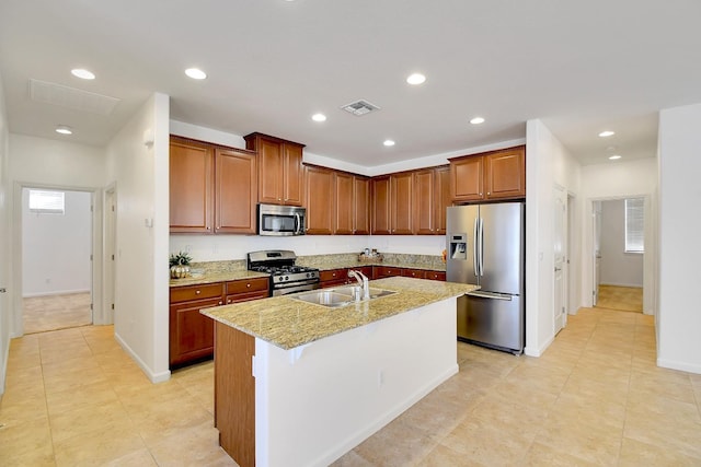 kitchen featuring light stone countertops, stainless steel appliances, sink, and an island with sink