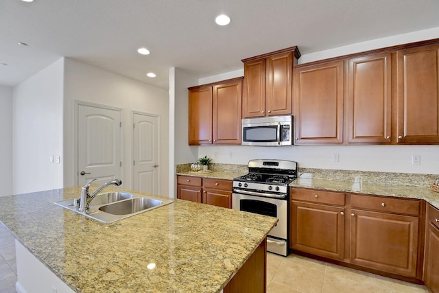 kitchen with sink, light tile floors, light stone counters, appliances with stainless steel finishes, and a center island with sink