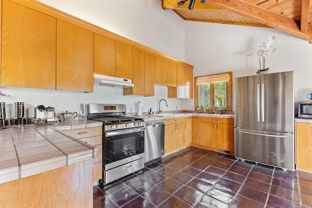 kitchen featuring beam ceiling, wooden ceiling, appliances with stainless steel finishes, dark tile floors, and tile counters