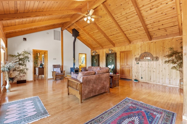 living room featuring high vaulted ceiling, ceiling fan, a wood stove, and beamed ceiling