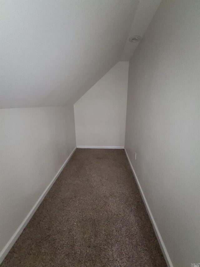 additional living space with dark colored carpet and vaulted ceiling