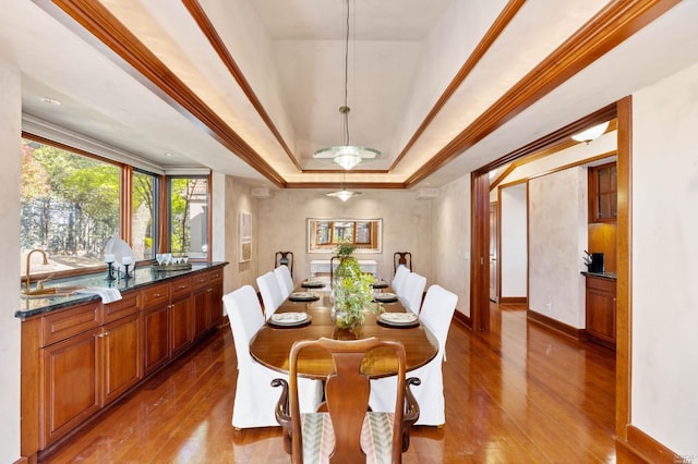 dining room featuring a tray ceiling, ornamental molding, hardwood / wood-style floors, and sink