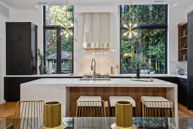 kitchen with an island with sink, pendant lighting, and light stone countertops