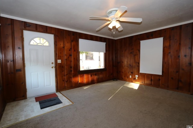 foyer with ceiling fan, wooden walls, and light colored carpet