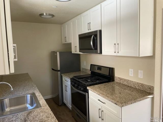 kitchen with stainless steel appliances, white cabinetry, sink, dark hardwood / wood-style floors, and light stone counters