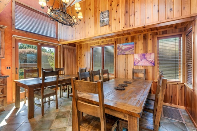 tiled dining area with an inviting chandelier, wood walls, and a high ceiling