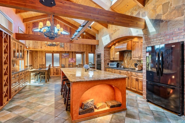 kitchen featuring black appliances, an inviting chandelier, a breakfast bar, an island with sink, and dark stone countertops