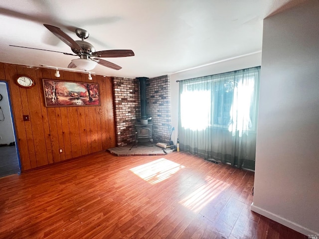 empty room featuring wooden walls, dark hardwood / wood-style floors, ceiling fan, and a wood stove