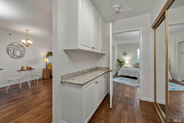 kitchen with an inviting chandelier, dark wood-type flooring, light stone counters, white cabinets, and pendant lighting