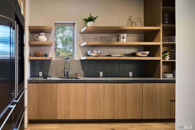 kitchen with high quality fridge, backsplash, a sink, open shelves, and dark countertops