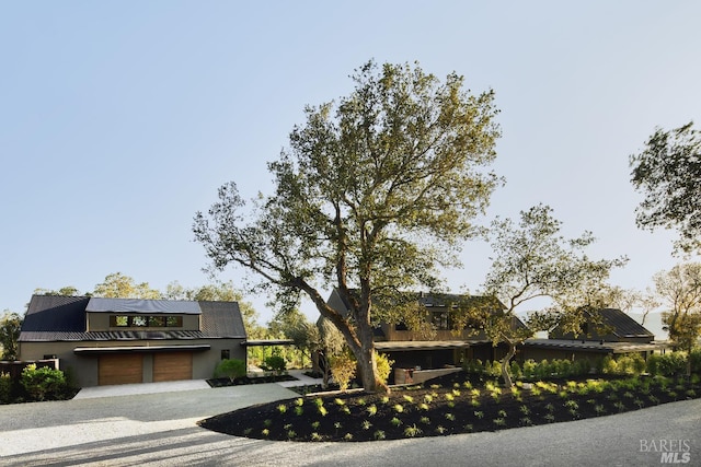 view of front of property with roof mounted solar panels, driveway, a garage, and metal roof