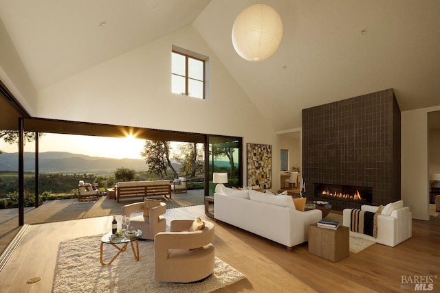 living room with high vaulted ceiling, a tiled fireplace, wood finished floors, and a mountain view