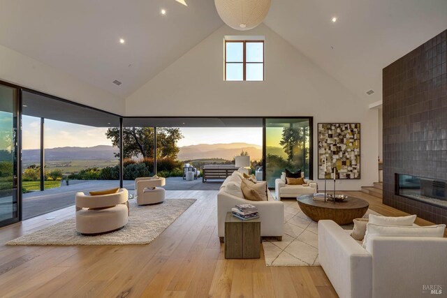 living area with high vaulted ceiling, visible vents, light wood finished floors, a fireplace, and a mountain view