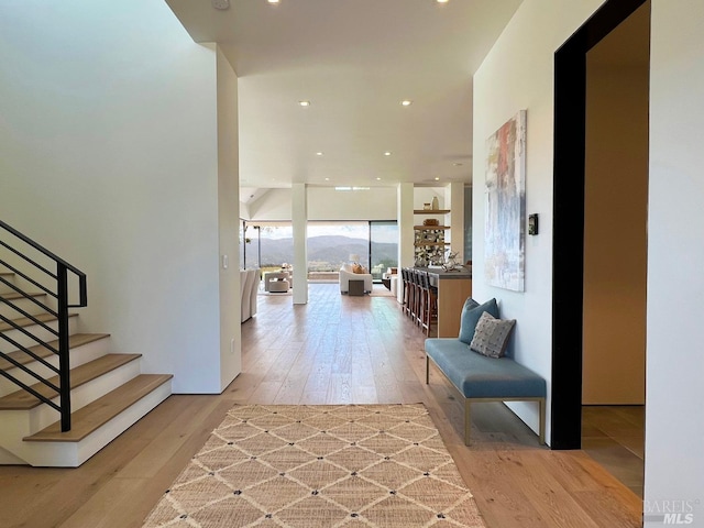 hallway featuring light wood finished floors, stairs, floor to ceiling windows, and recessed lighting