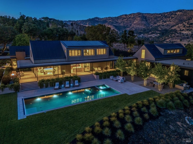 rear view of house with a mountain view, roof mounted solar panels, a yard, and a patio area