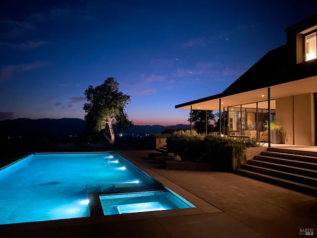 pool at dusk with a patio and a pool with connected hot tub