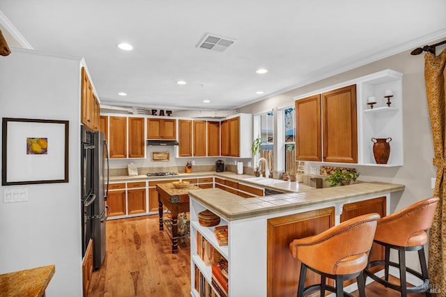 kitchen with kitchen peninsula, ornamental molding, a breakfast bar, and light hardwood / wood-style flooring