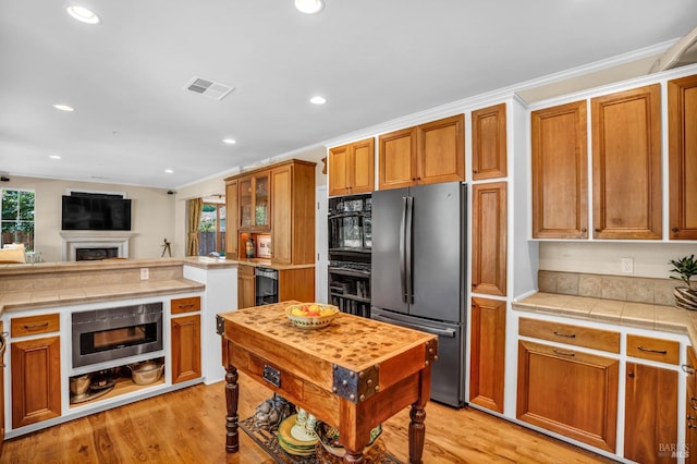 kitchen featuring tile countertops, double oven, light hardwood / wood-style floors, and stainless steel refrigerator