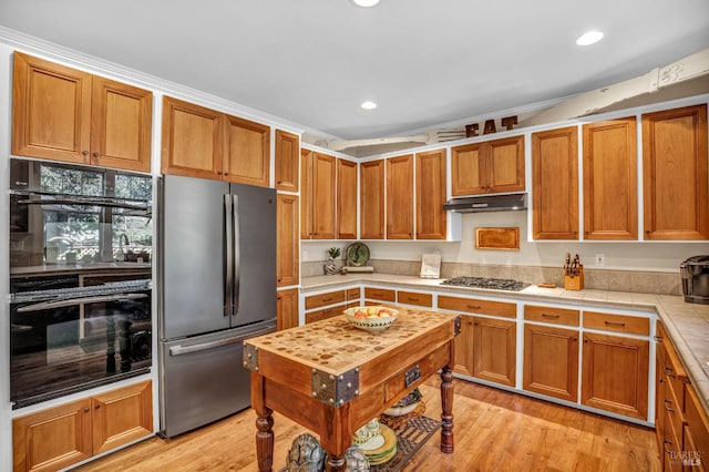 kitchen with ornamental molding, tile countertops, light hardwood / wood-style floors, and stainless steel appliances