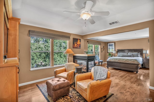 bedroom with ornamental molding, ceiling fan, light wood-type flooring, and a multi sided fireplace