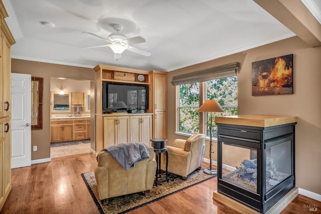 living room featuring ceiling fan, a multi sided fireplace, light hardwood / wood-style flooring, and ornamental molding