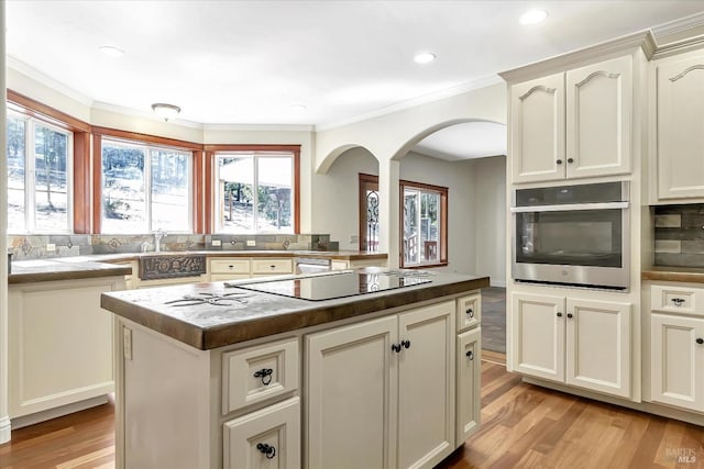 kitchen with light hardwood / wood-style floors, black electric stovetop, ornamental molding, oven, and a kitchen island