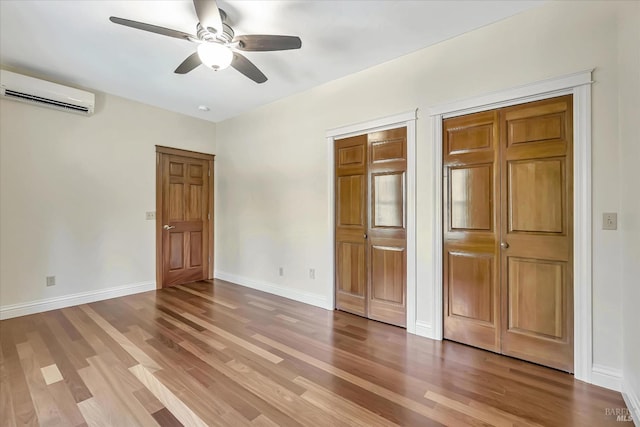 unfurnished bedroom featuring ceiling fan, two closets, a wall unit AC, and wood-type flooring