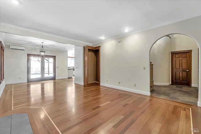 unfurnished living room with an AC wall unit, crown molding, hardwood / wood-style floors, and french doors