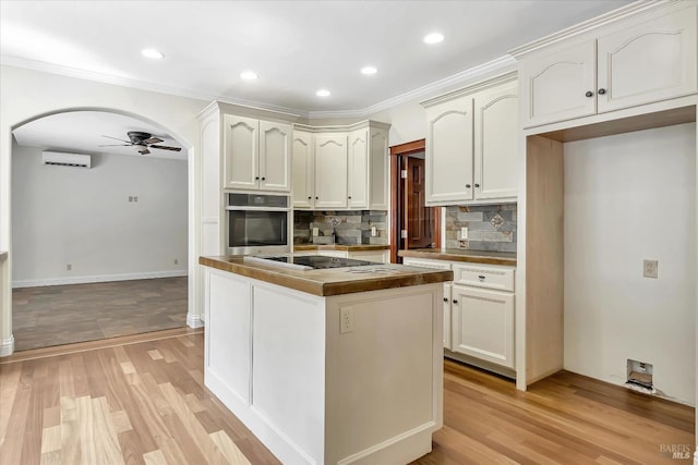 kitchen featuring stainless steel oven, black electric stovetop, light wood-type flooring, tasteful backsplash, and ceiling fan