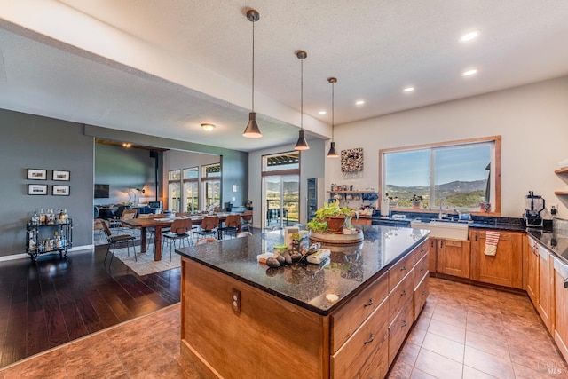 kitchen with decorative light fixtures, sink, light hardwood / wood-style flooring, dark stone countertops, and a kitchen island