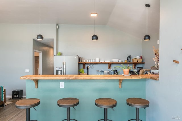 kitchen with stainless steel fridge, wood counters, a breakfast bar area, decorative light fixtures, and lofted ceiling