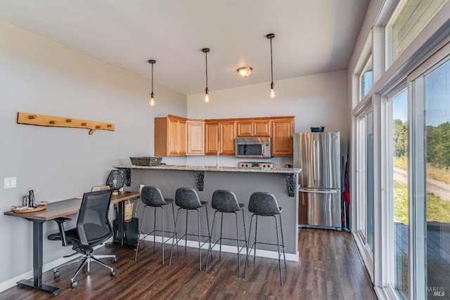 kitchen featuring stainless steel appliances, light stone countertops, a breakfast bar area, hanging light fixtures, and dark hardwood / wood-style floors