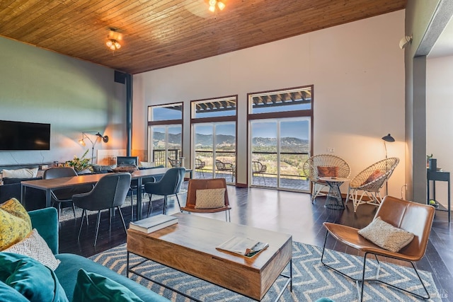 living room with a towering ceiling, a mountain view, dark wood-type flooring, and wooden ceiling