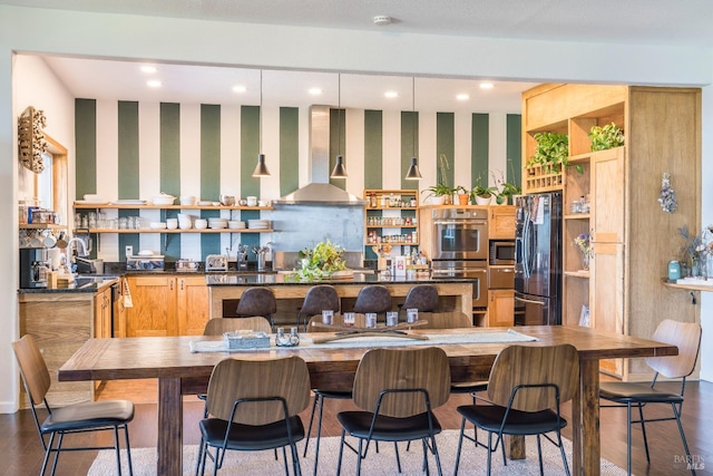 kitchen with wall chimney exhaust hood, dark hardwood / wood-style flooring, a kitchen breakfast bar, and appliances with stainless steel finishes