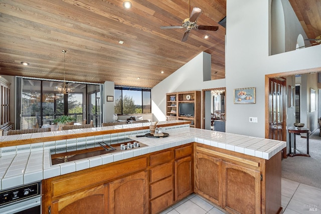 kitchen with kitchen peninsula, ceiling fan with notable chandelier, wooden ceiling, wall oven, and tile counters
