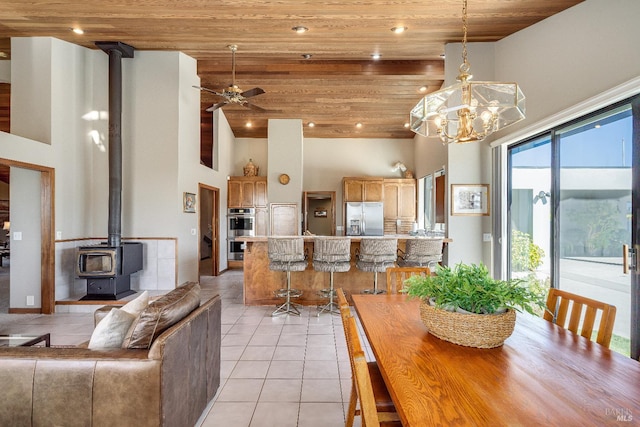 dining area featuring a wood stove, wood ceiling, light tile floors, and ceiling fan with notable chandelier