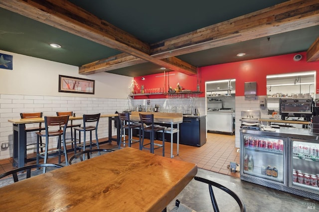 dining space with bar area, beamed ceiling, and light tile floors