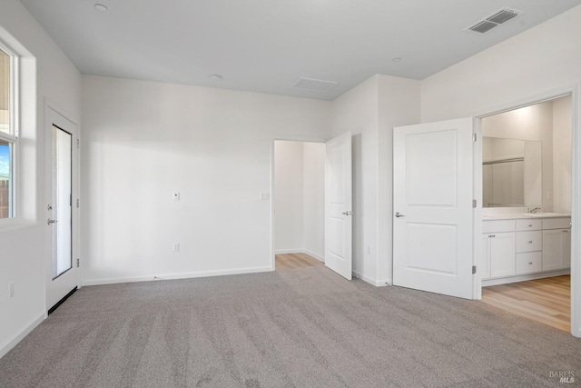 unfurnished bedroom featuring light carpet, ensuite bathroom, multiple windows, and sink