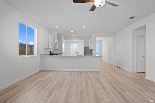 interior space with light wood-type flooring, ceiling fan, white cabinetry, and refrigerator