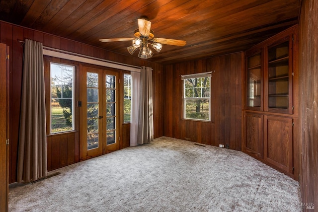 carpeted empty room with ceiling fan, wooden walls, wooden ceiling, and french doors