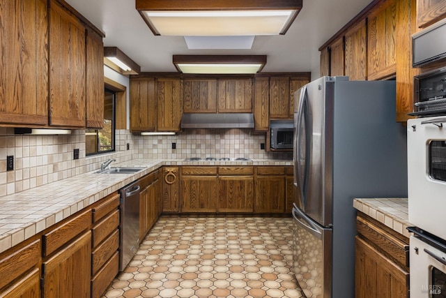 kitchen featuring backsplash, tile counters, appliances with stainless steel finishes, light tile patterned floors, and sink