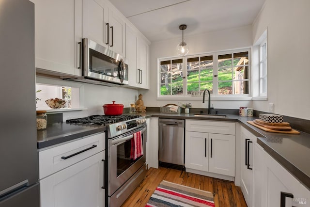 kitchen featuring appliances with stainless steel finishes, sink, hanging light fixtures, light wood-type flooring, and white cabinetry