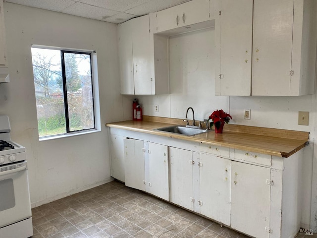 kitchen with sink, a paneled ceiling, white gas range, and white cabinets