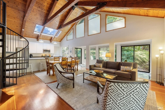 living room featuring high vaulted ceiling, light hardwood / wood-style flooring, plenty of natural light, and a skylight