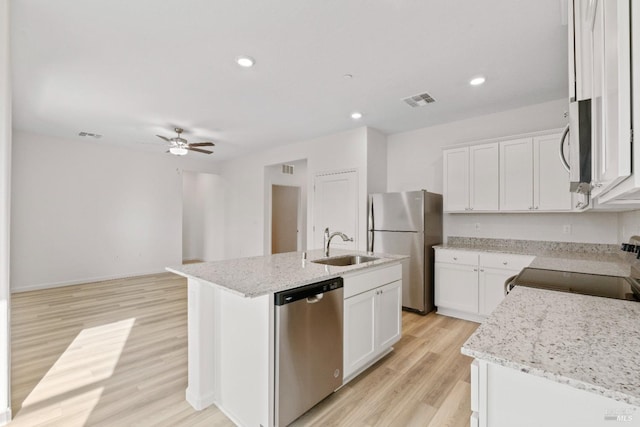 kitchen with appliances with stainless steel finishes, light hardwood / wood-style floors, an island with sink, light stone countertops, and ceiling fan