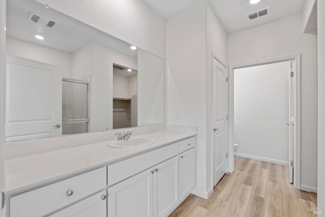 bathroom featuring a shower with door, vanity, hardwood / wood-style floors, and toilet