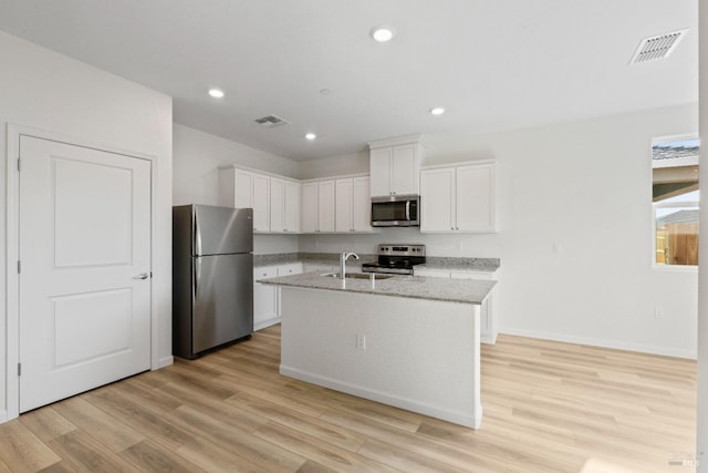kitchen with stainless steel appliances, a center island with sink, light stone counters, and light hardwood / wood-style flooring