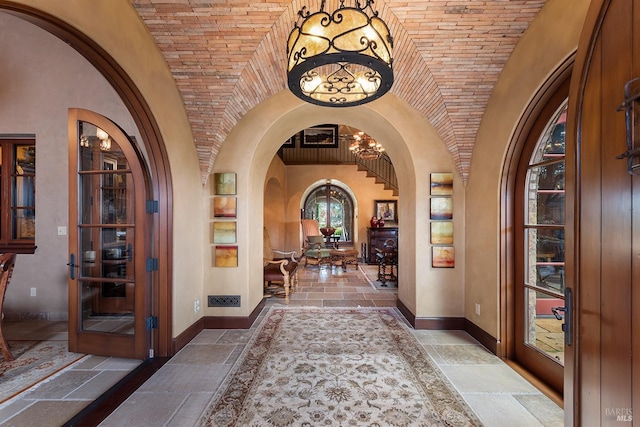 tiled foyer entrance with lofted ceiling, a chandelier, and brick ceiling